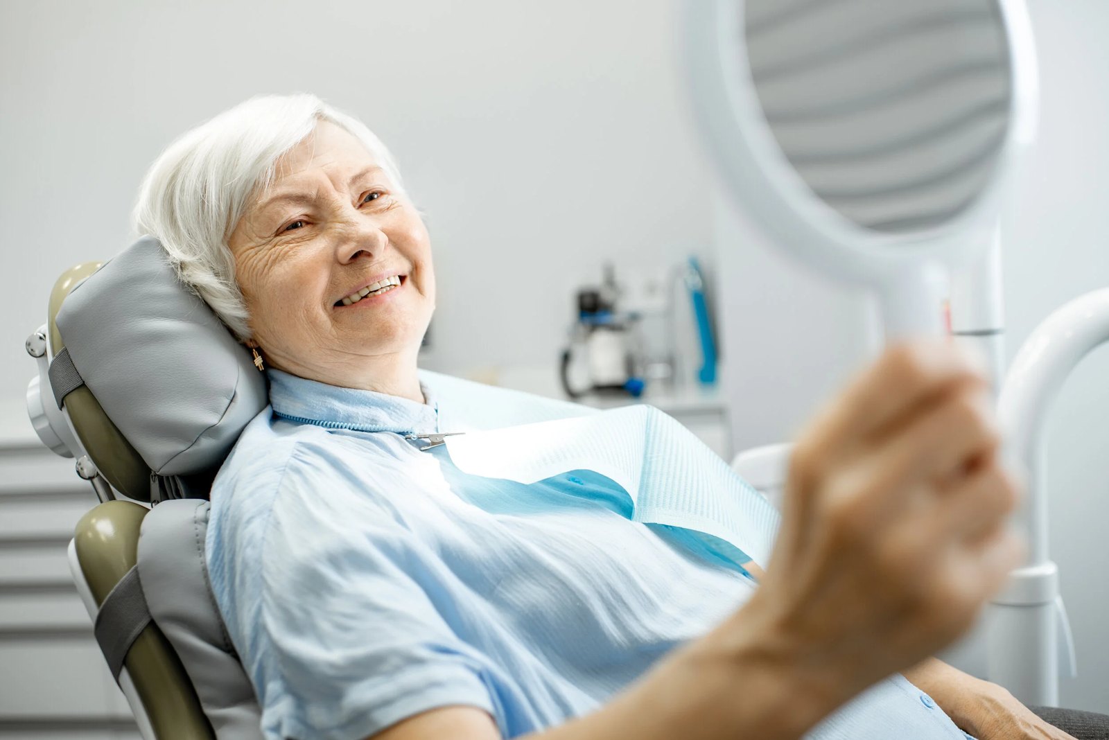 An adult looking in a handheld mirror at a dental visit